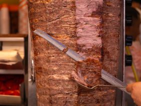 Close-up of a chef cutting meat with a doner knife for a traditional street food doner kebab or shawarma. Concept of street food