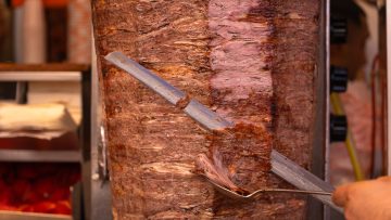 Close-up of a chef cutting meat with a doner knife for a traditional street food doner kebab or shawarma. Concept of street food