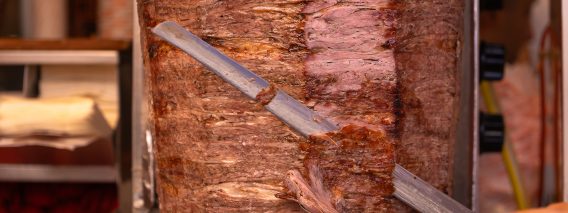 Close-up of a chef cutting meat with a doner knife for a traditional street food doner kebab or shawarma. Concept of street food